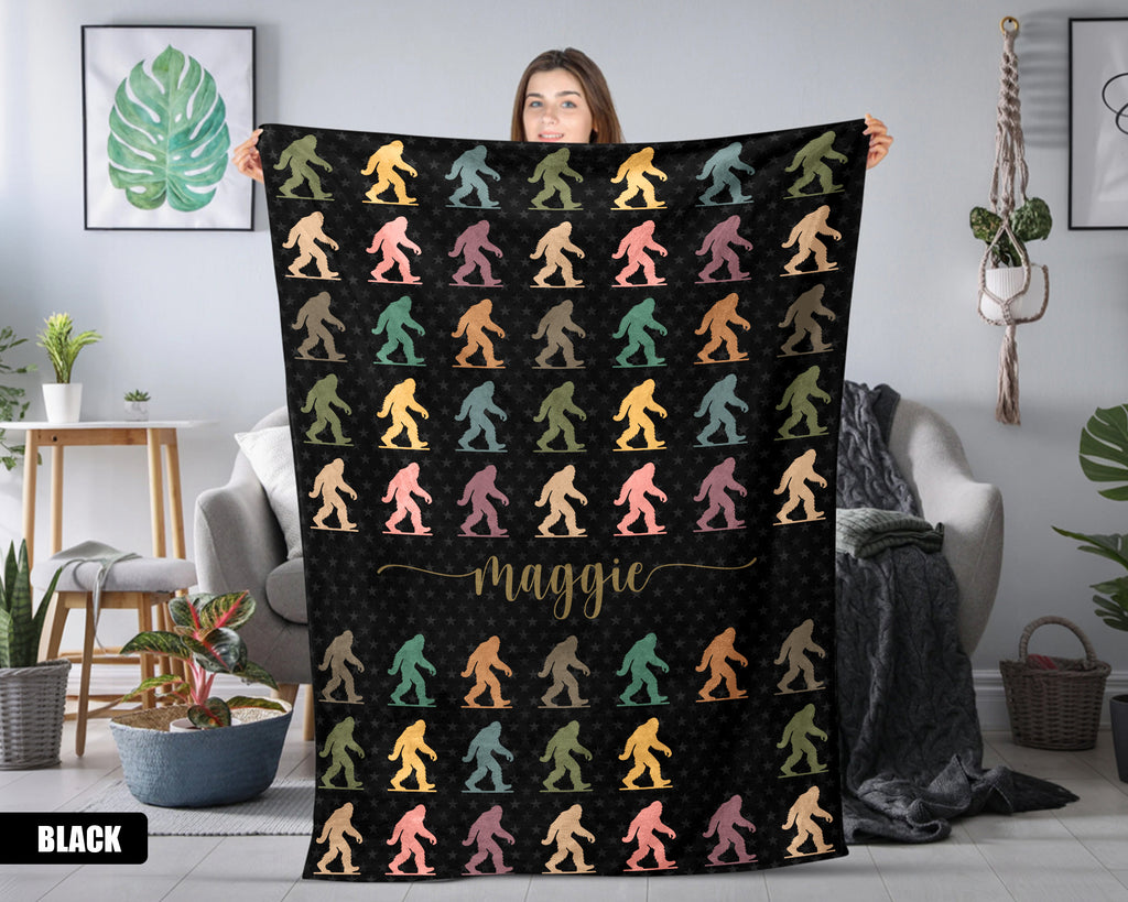 Person holding a black blanket with colorful 'bigfoot' pattern and name in a room.