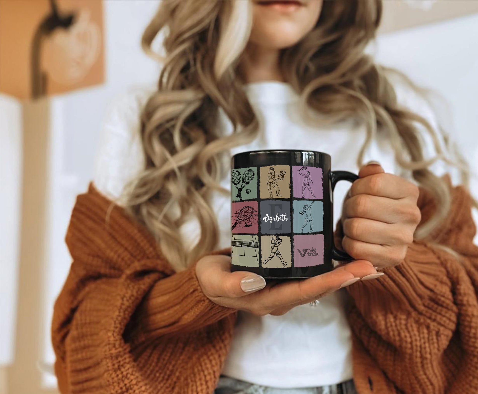 Person holding a black mug with colorful designs, wearing a brown sweater.
