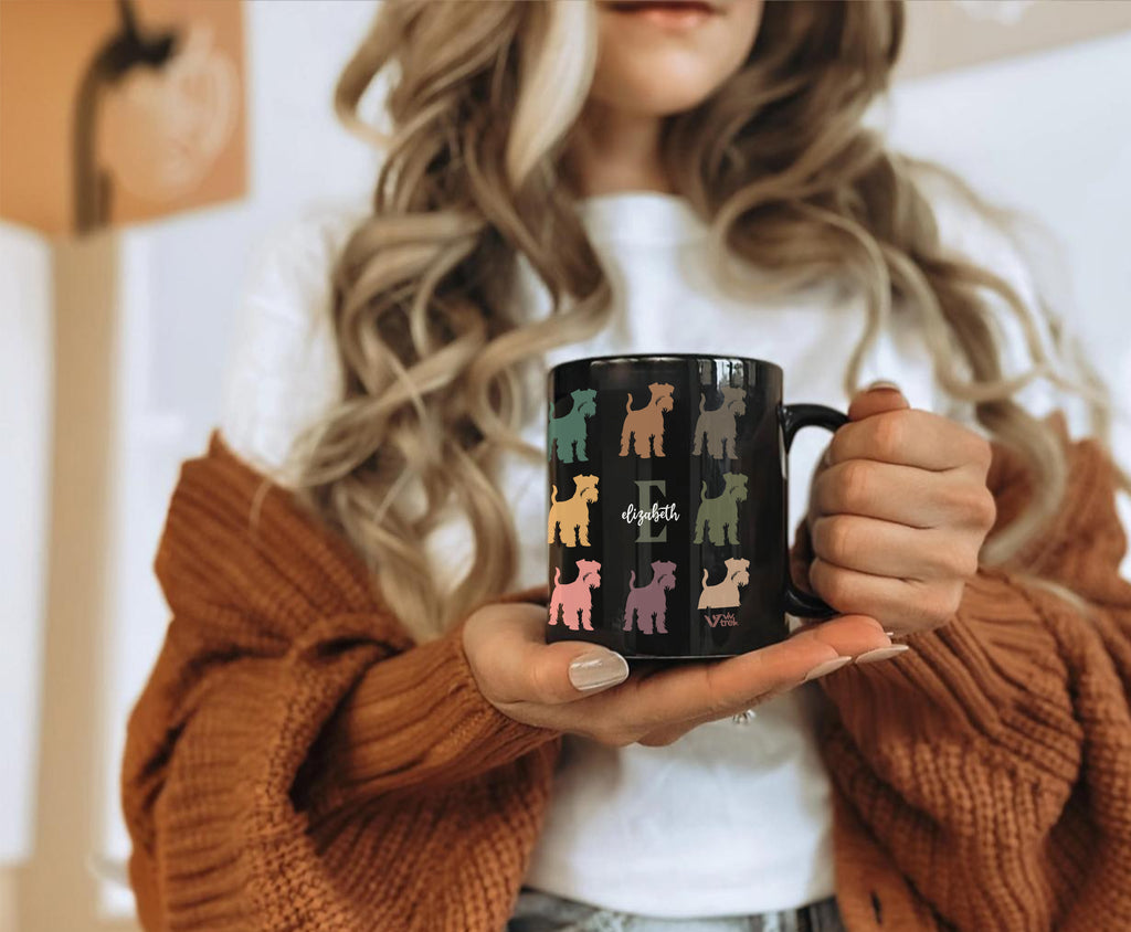 Person holding a black mug with colorful dog illustrations and the name text