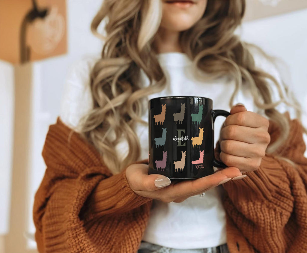 Person holding a black mug with colorful llama designs and the letter of name text.