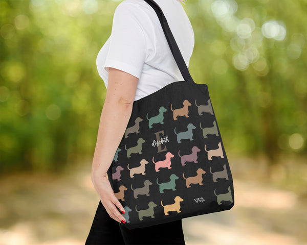 Person holding a black tote bag with dog pattern outdoors and name text