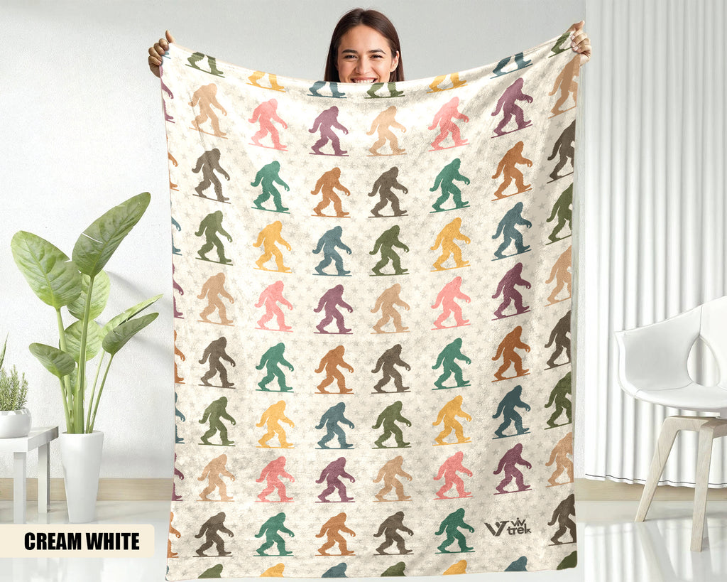 Person holding a blanket with colorful bigfoot pattern in a room with plants and furniture.