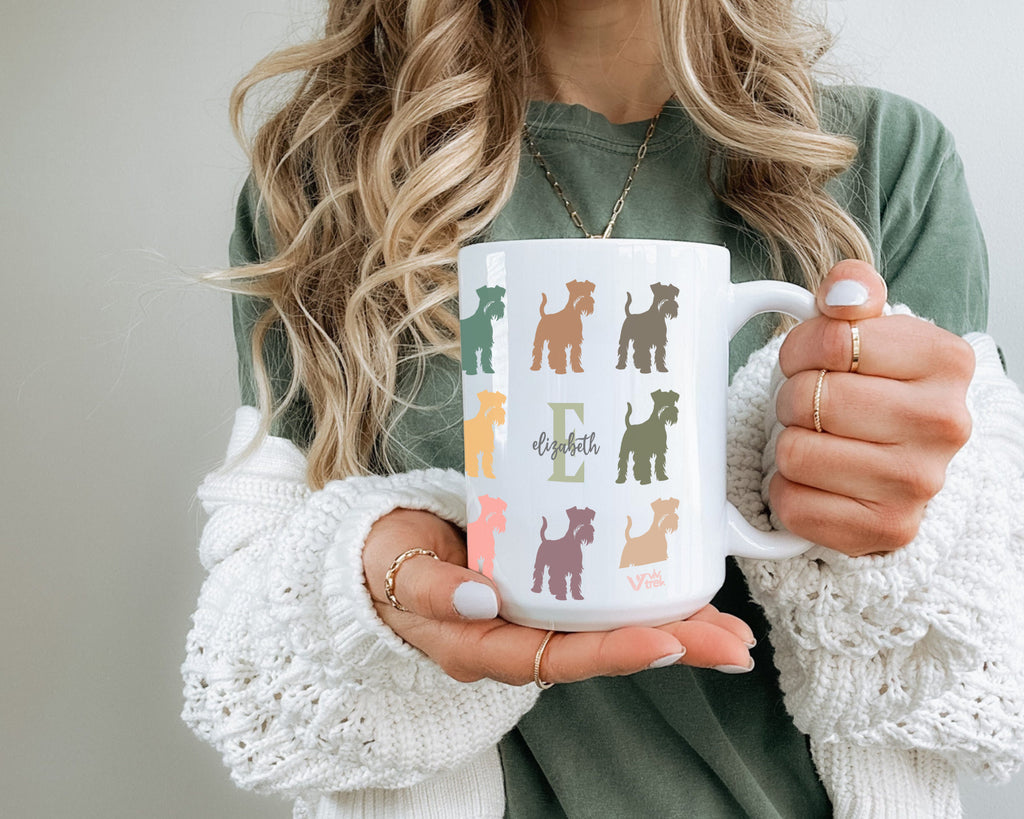 Person holding a mug with colorful dog illustrations and initial name text