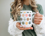 Person holding a mug with leaf pattern and name Text.